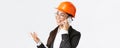 Close-up of professional smiling asian female entrepreneur at factory, chief engineer in safety helmet and suit, talking Royalty Free Stock Photo