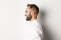 Close-up profile shot of handsome bearded man looking left and smiling, standing against white background Royalty Free Stock Photo