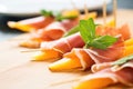 close-up of prosciutto slices between cantaloupe wedges with mint