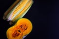 Close up pumpkins and corn on dark background with copy space. Half orange pumpkin and ripe corn cobs, top view Royalty Free Stock Photo