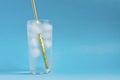Close up of pure water with ice and gold paper straw in tall transparent glass and sun glare on blue  background. Copy space Royalty Free Stock Photo