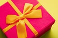 Close-up of a purple gift box with a yellow ribbon tied with a bow on a yellow background Royalty Free Stock Photo