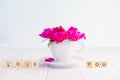 Close up purple pink peony flowers bouquet in a decorative cup and saucer and message I love you spelled in wooden blocks on white