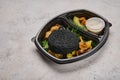 Close up rabbit cutlet in black breading in baby potatoes, spinach and mushrooms in black plastic container on light