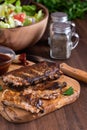 Close up of a rack of spareribs on a wooden board surrounded by barbecue sauce and a salad in behind.