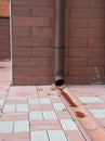 Close up on rain gutter downspout pipe for roof runoff with open water drainage in the pavement.