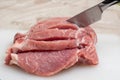 Close-up raw pork meat cut with a knife into several steaks on a cutting white board on the kitchen table Royalty Free Stock Photo