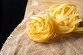 Close-up of raw tagliatelle nests on burlap and rustic wooden table, black background,