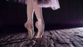 close up, in rays of spotlight, on stage of old theater hall. ballerina in white ballet skirt, raises on toes in pointe