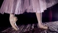 close up, in rays of spotlight, on stage of old theater hall. ballerina in white ballet skirt, raises on toes in pointe