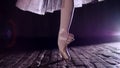 close up, in rays of spotlight, on stage of old theater hall. ballerina in white ballet skirt, rotates on toe in pointe