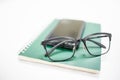 Close up of reading glasses on mobile smartphone and green notebook on white table. Education technology and work concept Royalty Free Stock Photo