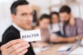 Close up. Realtor holds in hand white card with inscription by realtor, with family who buys house.