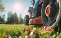 Close-up of a red and black lawn mower cutting lush green grass. The mower has a large orange wheel. Royalty Free Stock Photo