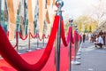 Close up red carpet ceremony with selective focus on the stanchions and the ropes with blurred guests and photographer background.