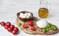 Close-up of red cherry tomatoes with white mozzarella cheese, olive oil and green leaves of basil on white wooden background. Royalty Free Stock Photo