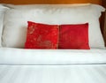 Close up A red Chinese style fabric scatter cushion, backrest pillow, placed in front of double white pillows on the hotel bed,