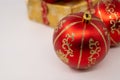 Close-up of a red Christmas bulb with golden stripes on it. Golden gift box in background. Isolated white background Royalty Free Stock Photo