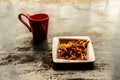 Close up Red Color Coffee mug and white plate full of Namkeen Bhujia snack cookies on old rustic floor. Food and drink background Royalty Free Stock Photo