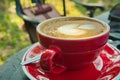 Close up a red cup of tasty coffee with heart-shaped latte art foam on a table Royalty Free Stock Photo