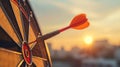 Close up red dart arrow hitting target center dartboard on sunset background. Business targeting and focus concept. Royalty Free Stock Photo