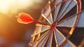 Close up red dart arrow hitting target center dartboard on sunset background. Business targeting and focus concept. Royalty Free Stock Photo