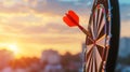 Close up red dart arrow hitting target center dartboard on sunset background. Business targeting and focus concept. Royalty Free Stock Photo