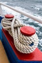 Close up of red double bollard with rope tied around it, ship detail against ocean water Royalty Free Stock Photo