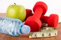 Close up of red dumbbell, water in bottle, green fresh apple with dew and measuring tape on wooden floor Royalty Free Stock Photo