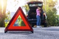 Close up red emergency stop sign standing on road. Worried and angry woman walking near his broken car talking on phone with Royalty Free Stock Photo