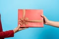 Close-up of a red gift box in the hands of two women. Box handles on each side. Second hand sent a gift box tied with a beautiful Royalty Free Stock Photo