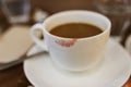 Close up of red lipstick smudges on hot latte in white coffee cup on wood table near window in coffee shop in the morning in Royalty Free Stock Photo