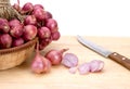 Close up red onion or shallots in wooden basket with sliced onion on wooden chopping block