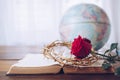 Close up of the red rose with the crown of thorns on an old open bible on wooden table