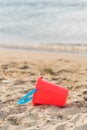 Child`s red sand pail lying on sandy beach with water in background Royalty Free Stock Photo