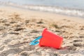 Close-up of red sand pail lying on sandy beach with waves in background in summer Royalty Free Stock Photo