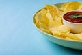 Close-up of red sauce in bowl amidst potato chips served in plate on blue background with copy space
