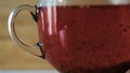 Close-up of red tea brewing in transparent mug. Concept. Tea turns boiling water red. Beautiful red tea brewed on wooden