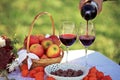 Close up of red wine being poured from bottle to glass, picnic in the nature, a basket of apples, chocolate candies