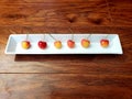 Close up on six spaced out red and yellow cherries on a white plate