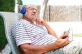 Close-up of a retired man with a thoughtful face wearing blue headphones sitting on a lawn chair Royalty Free Stock Photo