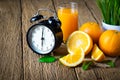 Close-up of Retro clock vintage with glass orange juice and fresh fruits ripe cut half, slice with green leaves on old wood table. Royalty Free Stock Photo