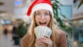 Close up rich Caucasian happy success woman lady in red Santa Christmas hat cap and eyeglass holding money dollars cash Royalty Free Stock Photo