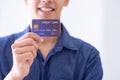 Close-up of the right hand of a young man holding a blue credit card, seeing a smile but not seeing the face clearly
