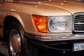 Close-up of the right headlight of retro beige car with chrome radiator, bumper, disk and light alloy wheels