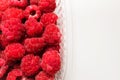 Close-up ripe juicy and delicious raspberry in a plastic transparent dish on a light background. Saturated healthy fresh