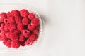 Close-up ripe juicy and delicious raspberry in a plastic transparent dish on a light background. Saturated healthy fresh