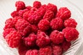 Close-up ripe juicy and delicious raspberry in a plastic transparent dish on a light background. Saturated healthy fresh