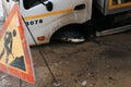Close-up of road accident truck falling into hole in asphalt, road sign of repair work. Selective focus on car wheel