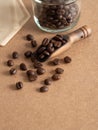 Close up, roasted coffee beans in wooden scoop with glass bottle and coffee filter on brown background.